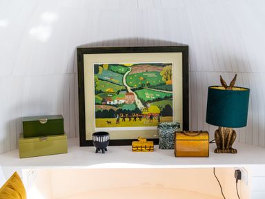 A shelf with a framed painting of a farm scene two green boxes two small decorative containers and a rabbit-shaped lamp with a teal shade at Veiko - Mayflower Meadow in Burshill near Brandesburton