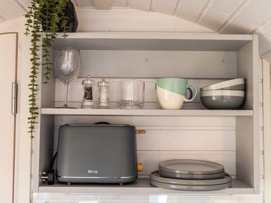 A kitchen shelf with a toaster plates bowls mugs wine glass and salt and pepper grinders at Veiko - Mayflower Meadow in Burshill near Brandesburton