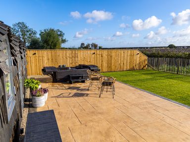 An outdoor patio with chairs a hot tub and potted plants next to a lawn at Veiko - Mayflower Meadow in Burshill near Brandesburton