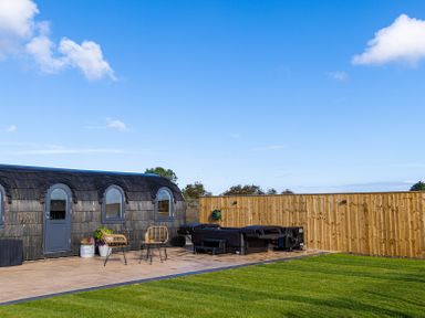 A wooden pod with arched windows and door near a patio with chairs and a hot tub and a wooden fence at Veiko - Mayflower Meadow in Burshill near Brandesburton