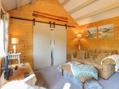 A living room with wood paneled walls a sofa and a tv at Willow Lodge in Potter Heigham