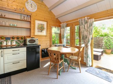 A wooden kitchen with a round dining table and chairs next to glass doors with curtains at Willow Lodge in Potter Heigham