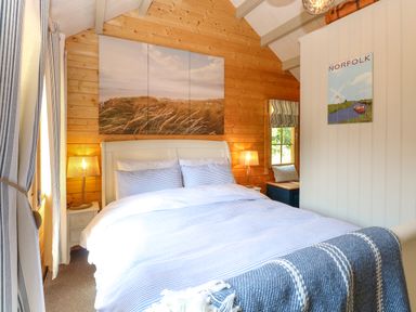 A bedroom with a bed and bedside lamps in a wooden cabin at Willow Lodge in Potter Heigham