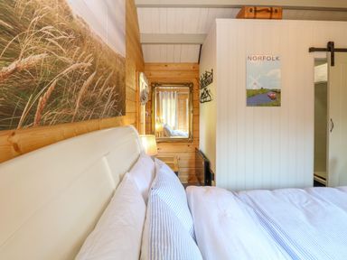 A bedroom with a bed with striped bedding a lamp a mirror a Norfolk poster and wooden walls at Willow Lodge in Potter Heigham