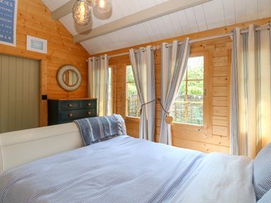 A bedroom with a bed a striped blanket curtains windows and a black chest of drawers at Willow Lodge in Potter Heigham