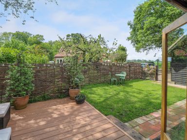 A garden with wooden decking potted plants green lawn a table with two chairs and a woven fence at Willow Lodge in Potter Heigham