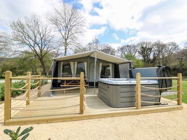 An outdoor wooden deck with a hot tub and a covered tent with a picnic table at The Otter in Nantmel near Rhayader