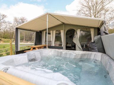 An outdoor hot tub in front of a large tent with picnic table and seating at The Otter in Nantmel near Rhayader
