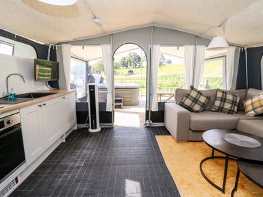 An open living space with a kitchen area and sofa with cushions next to a coffee table at The Otter in Nantmel near Rhayader