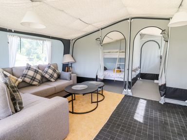 A tent interior with a grey sofa and cushions a floor lamp a pair of round tables and bunk beds at The Otter in Nantmel near Rhayader