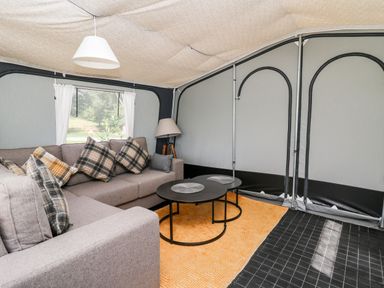 An interior of a tent with a gray sofa with plaid pillows two round black coffee tables a floor lamp and an orange patterned rug at The Otter in Nantmel near Rhayader