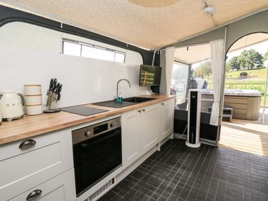 A kitchen with white cabinets and a wooden countertop beside a window and an outdoor view at The Otter in Nantmel near Rhayader