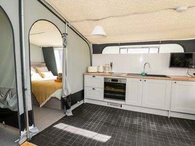 A kitchen area with white cabinets and wooden countertop open to a bedroom with a bed at The Otter in Nantmel near Rhayader
