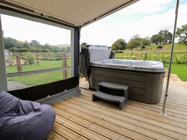 A hot tub with steps on a wooden deck outside with grass and trees at The Otter in Nantmel near Rhayader