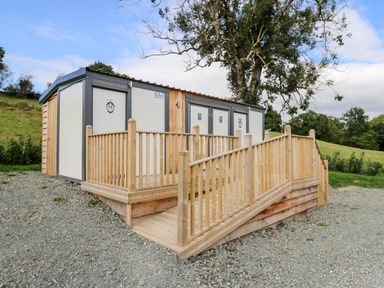 A public restroom building with wooden ramp and railings in a grassy outdoor area at The Otter in Nantmel near Rhayader