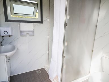 A bathroom with a small window sink paper dispenser shower with curtain and toilet at The Otter in Nantmel near Rhayader