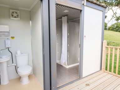 A small bathroom with a toilet and sink next to a shower area on a wooden deck outside at The Otter in Nantmel near Rhayader