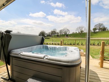 An outdoor hot tub with water bubbling on a wooden deck overlooking a grassy field and trees at The Otter in Nantmel near Rhayader