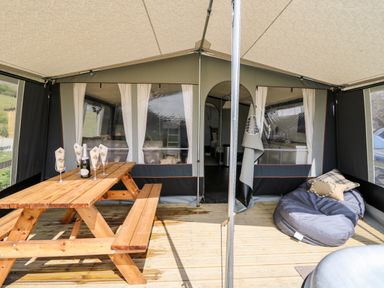 A tented space with a wooden picnic table holding glasses and a bottle and a bean bag with pillows at The Otter in Nantmel near Rhayader