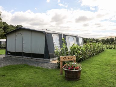 A large gray and black tent on a grassy area with shrubs and a wooden sign that says Otter at The Otter in Nantmel near Rhayader