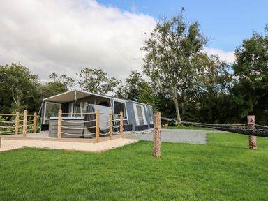 An outdoor tent with a wooden deck and hot tub surrounded by trees and grass at The Otter in Nantmel near Rhayader