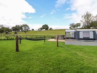 A grassy backyard with a hammock between wooden posts near a large tent at The Otter in Nantmel near Rhayader