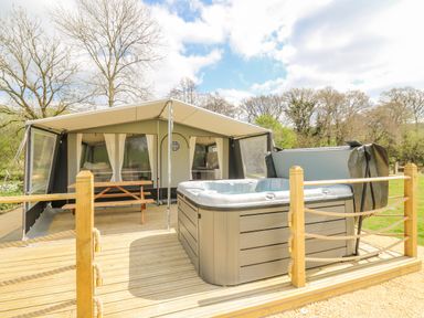 A wooden deck with hot tub and picnic table outside a tent in a wooded area at The Heron in Nantmel near Rhayader