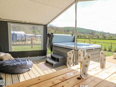 A covered outdoor area with a hot tub wooden table with glasses and napkins and a bean bag at The Heron in Nantmel near Rhayader