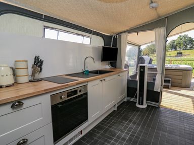 A kitchen with white cabinets wooden countertop and a black oven next to a window and a door leading outside at The Heron in Nantmel near Rhayader