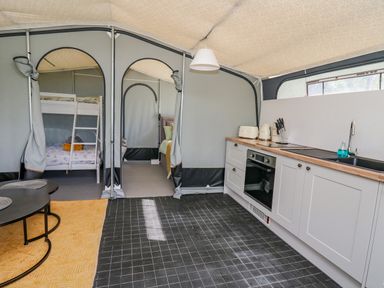 An interior of a tent with a kitchen area featuring white cabinets and appliances and a sleeping area with bunk beds at The Heron in Nantmel near Rhayader