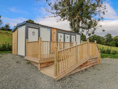 A wooden ramp and deck leading to public restroom doors in an outdoor grassy area at The Heron in Nantmel near Rhayader