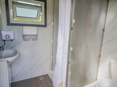 A bathroom with a sink a toilet a shower with a curtain a window and a paper towel dispenser at The Heron Nantmel near Rhayader