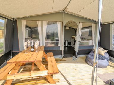 An outdoor tented area with a wooden picnic table set with glasses and a bottle and a bean bag chair at The Heron in Nantmel near Rhayader
