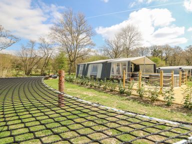 A large tent with a wooden deck and hot tub surrounded by grass and trees at The Heron in Nantmel near Rhayader