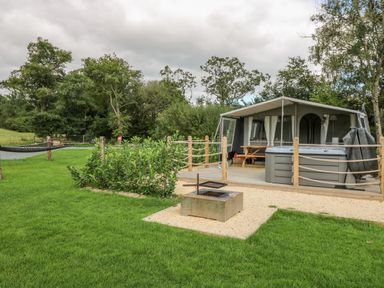 An outdoor camping area with a tent, picnic table, hot tub, fire pit, hammock, and green grass at The Heron in Nantmel near Rhayader