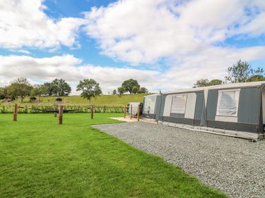 A large tent on a gravel area next to a grassy field with wooden posts and trees in the background at The Heron in Nantmel near Rhayader