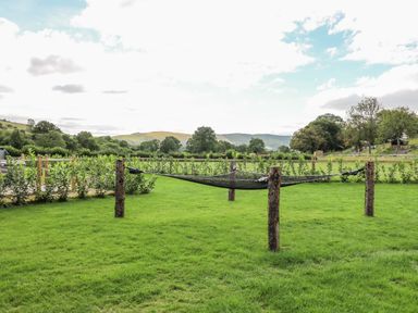 A grassy outdoor area with a net hammock supported by wooden posts at The Heron in Nantmel near Rhayader