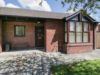 A brick house exterior with a dark front door, two windows, a bench, and a tiled patio at 21 Eamont Park Penrith