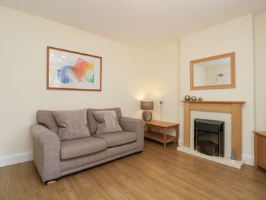 A living room with a sofa two cushions a wooden table lamp a fireplace and a mirror at 21 Eamont Park in Penrith