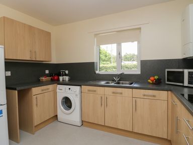 A kitchen with wooden cabinets a washing machine a sink a microwave and a window at 21 Eamont Park in Penrith