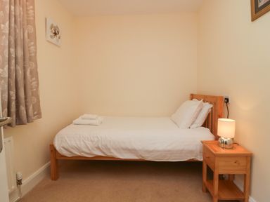 A small bedroom with a single bed a wooden nightstand with a lamp and folded towels on the bed at 21 Eamont Park in Penrith