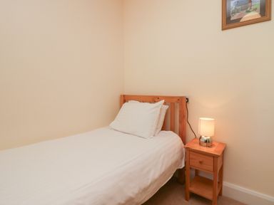 A single bed with white bedding a wooden bedside table with a lamp and a framed picture on the wall at 21 Eamont Park Penrith