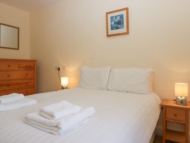 A bedroom with a double bed white bedding folded towels wooden bedside tables lamps dresser and framed picture on wall at 21 Eamont Park in Penrith