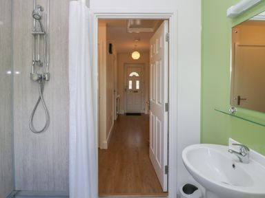 A bathroom with a shower and sink looking out to a hallway with a wooden floor at 21 Eamont Park in Penrith