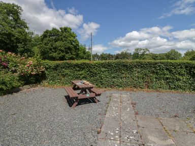 An outdoor area with a wooden picnic table on gravel and a hedge in the background at 21 Eamont Park in Penrith