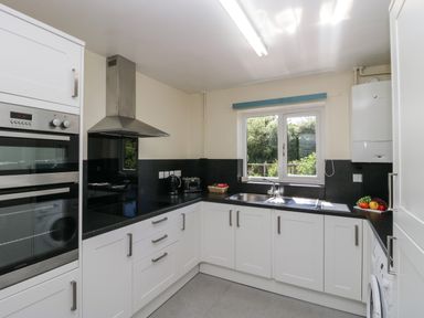 A kitchen with white cabinets black countertops a window a stainless steel oven cooker hood and small appliances at 12 Eamont Park in Penrith