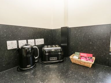 A kitchen counter with a black electric kettle black four slot toaster and a basket with tea bags at 12 Eamont Park in Penrith