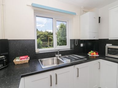 A kitchen sink under a window with a fruit plate on the counter and white cabinets at 12 Eamont Park in Penrith