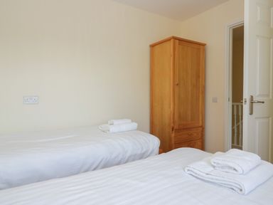 A bedroom with two single beds and a wooden wardrobe at 12 Eamont Park in Penrith