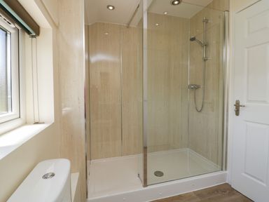 A bathroom with a glass shower enclosure a shower head a white toilet a window and a white door at 12 Eamont Park in Penrith